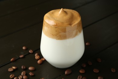 Photo of Delicious dalgona coffee in glass and beans on wooden table, closeup