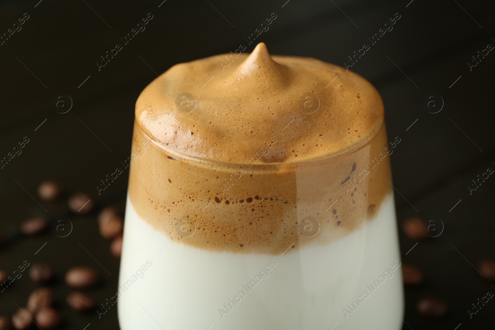 Photo of Delicious dalgona coffee in glass and beans on table, closeup
