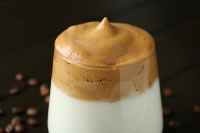 Photo of Delicious dalgona coffee in glass and beans on table, closeup