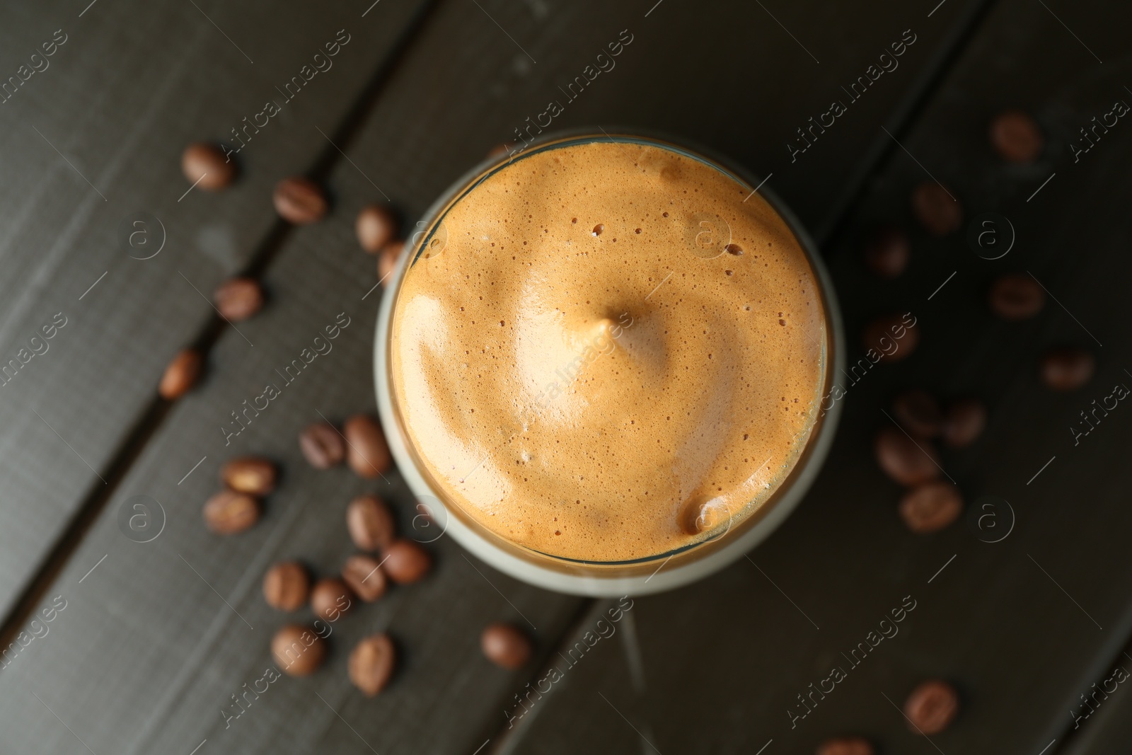Photo of Delicious dalgona coffee in glass and beans on wooden table, flat lay