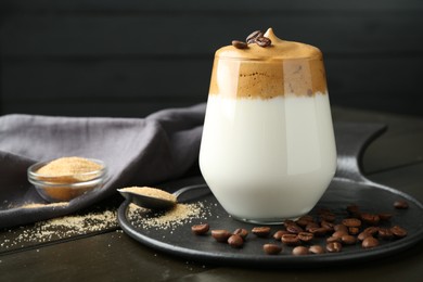 Photo of Delicious dalgona coffee in glass, beans and brown sugar on wooden table, closeup