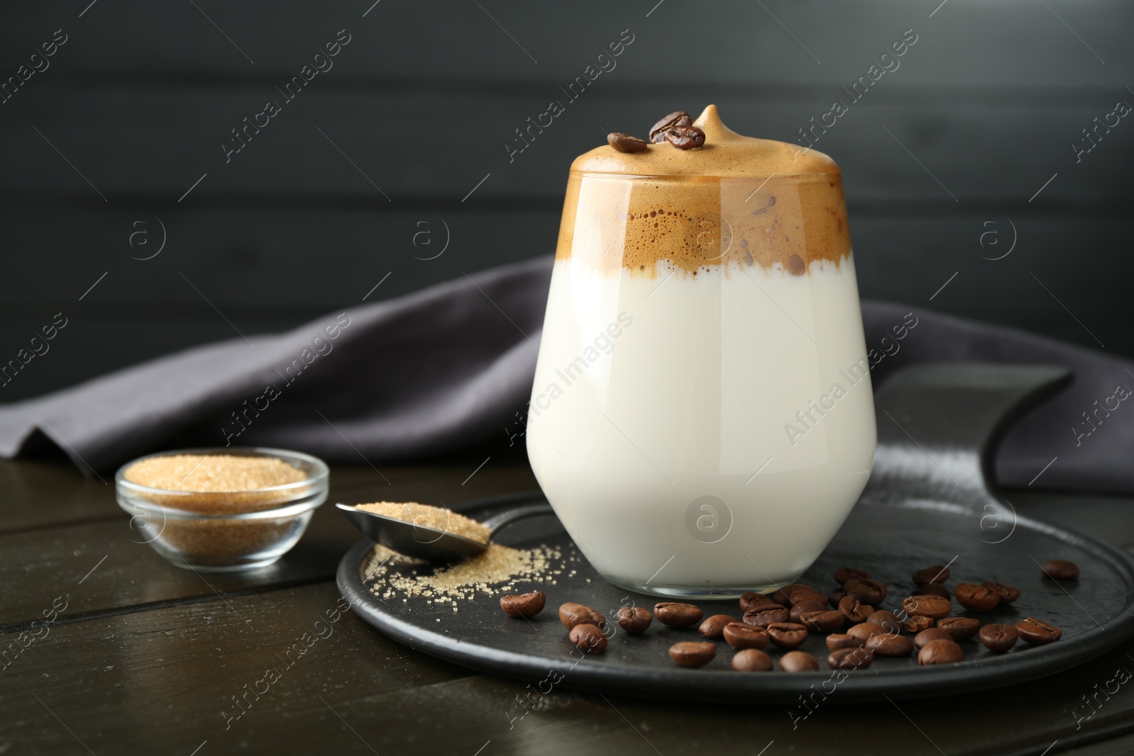 Photo of Delicious dalgona coffee in glass, beans and brown sugar on wooden table, closeup