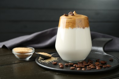 Photo of Delicious dalgona coffee in glass, beans and brown sugar on wooden table, closeup