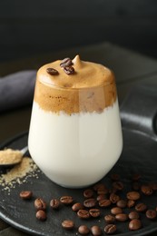 Photo of Delicious dalgona coffee in glass, beans and brown sugar on table, closeup