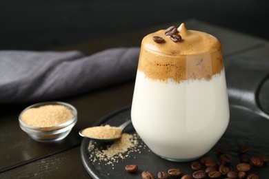 Photo of Delicious dalgona coffee in glass, beans and brown sugar on wooden table, closeup