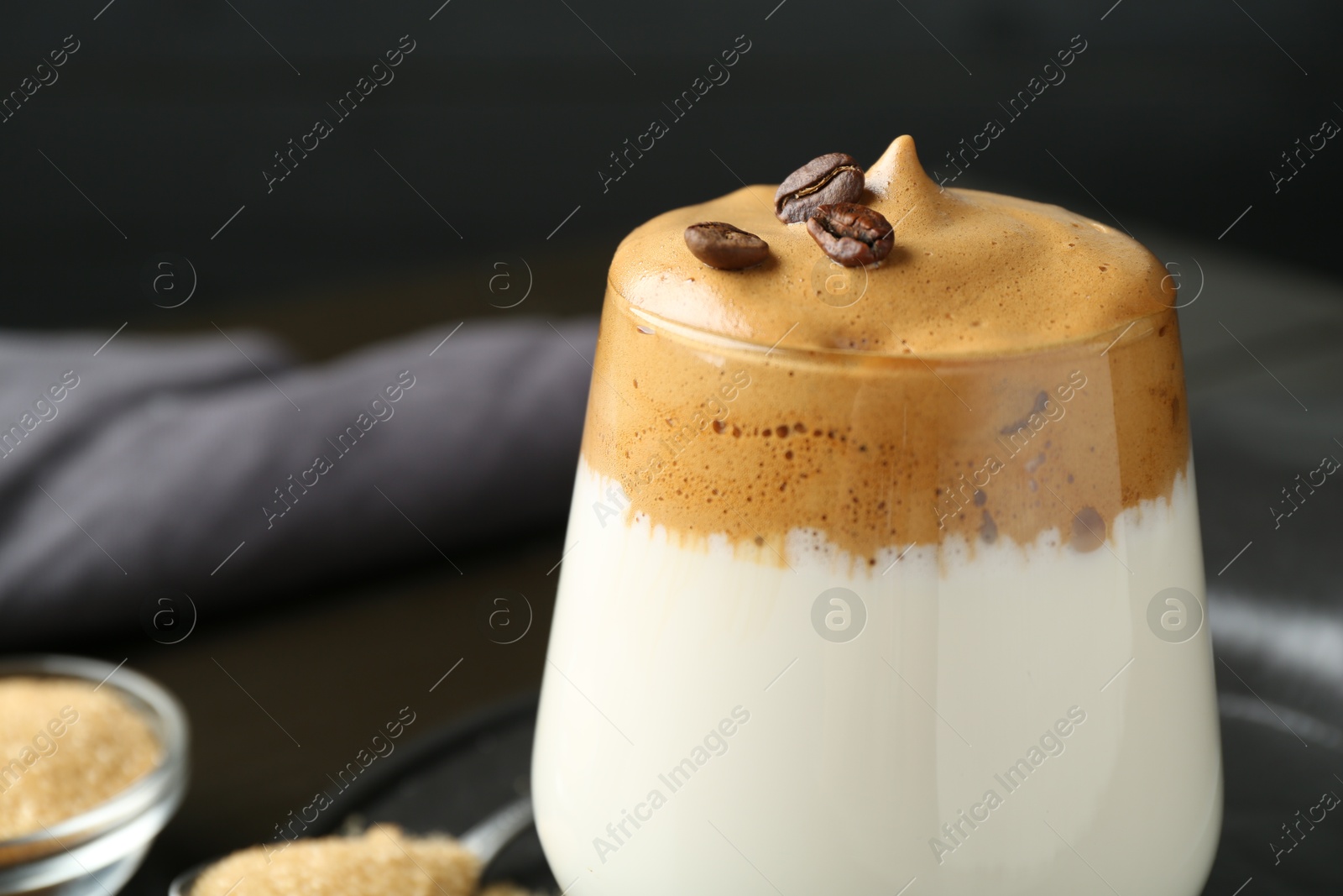 Photo of Delicious dalgona coffee in glass, beans and brown sugar on table, closeup. Space for text