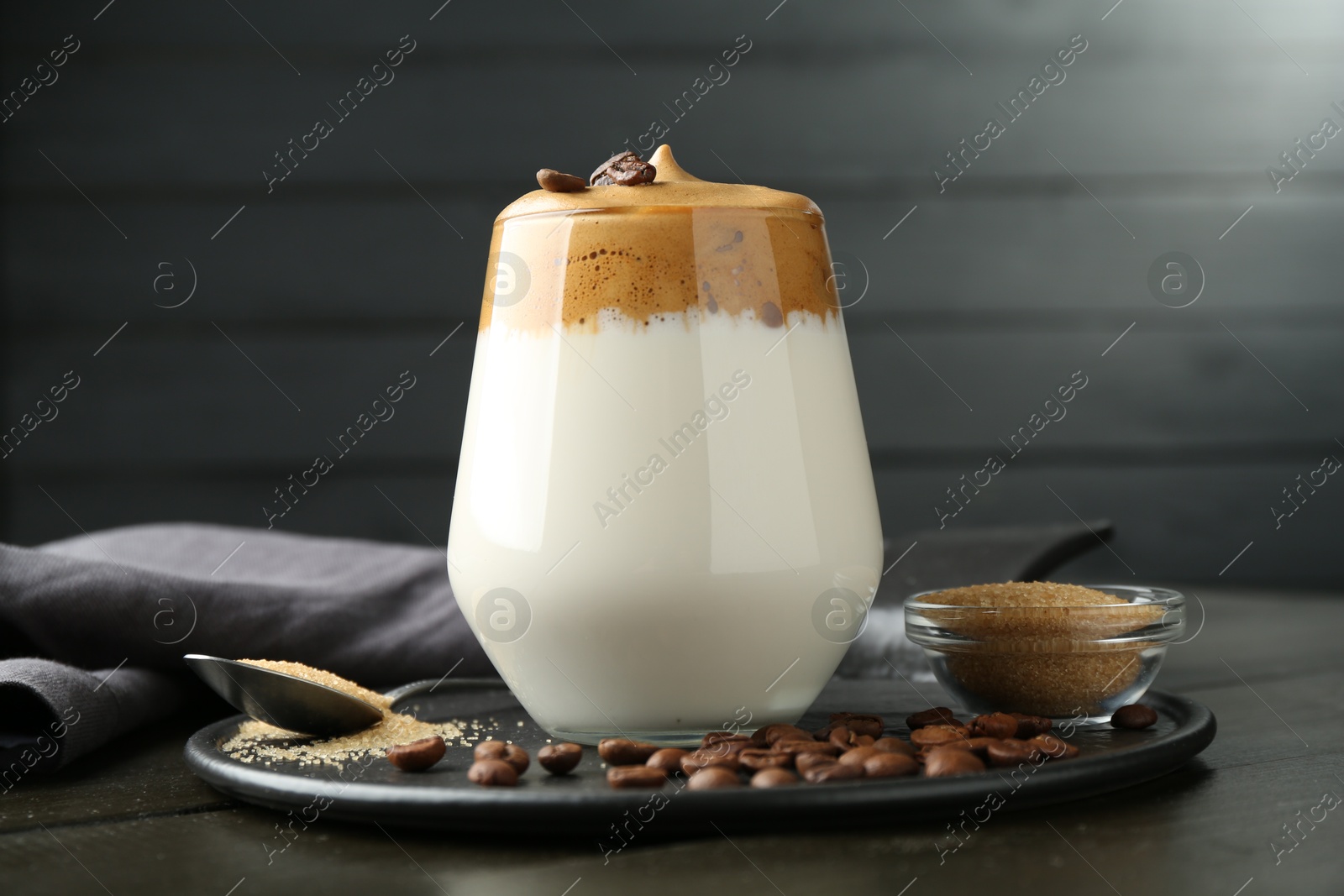 Photo of Delicious dalgona coffee in glass, beans and brown sugar on wooden table, closeup