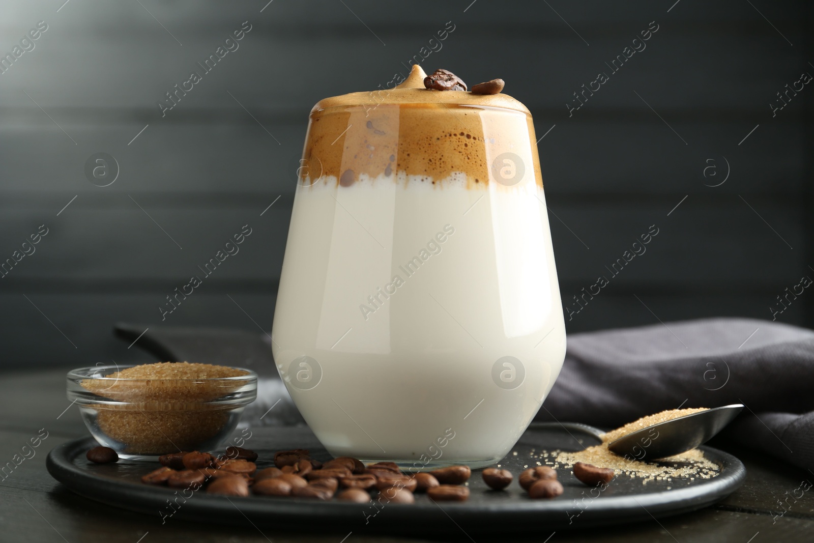 Photo of Delicious dalgona coffee in glass, beans and brown sugar on table, closeup