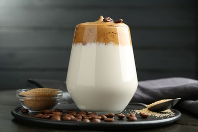 Photo of Delicious dalgona coffee in glass, beans and brown sugar on table, closeup