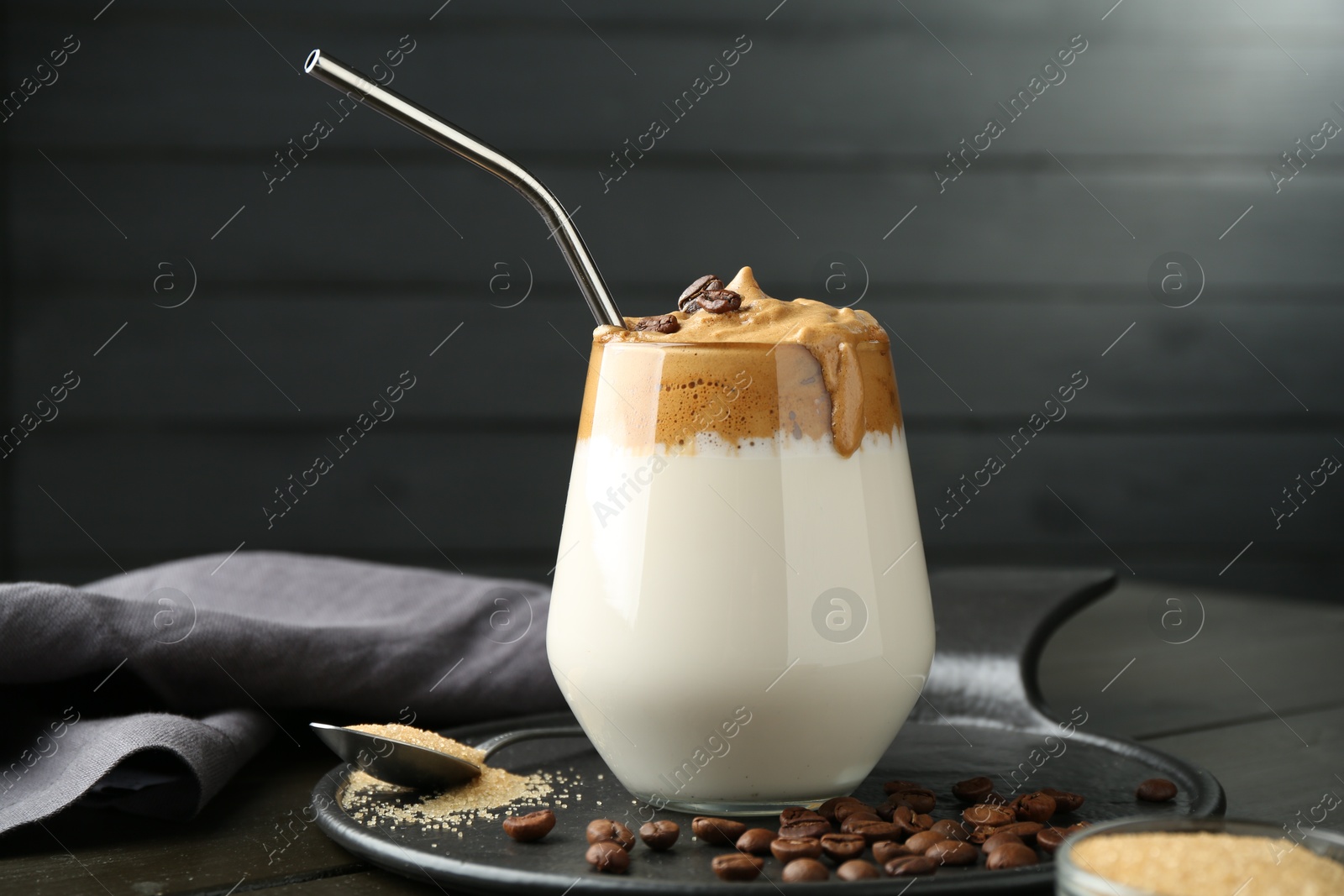Photo of Delicious dalgona coffee in glass, beans and brown sugar on wooden table, closeup