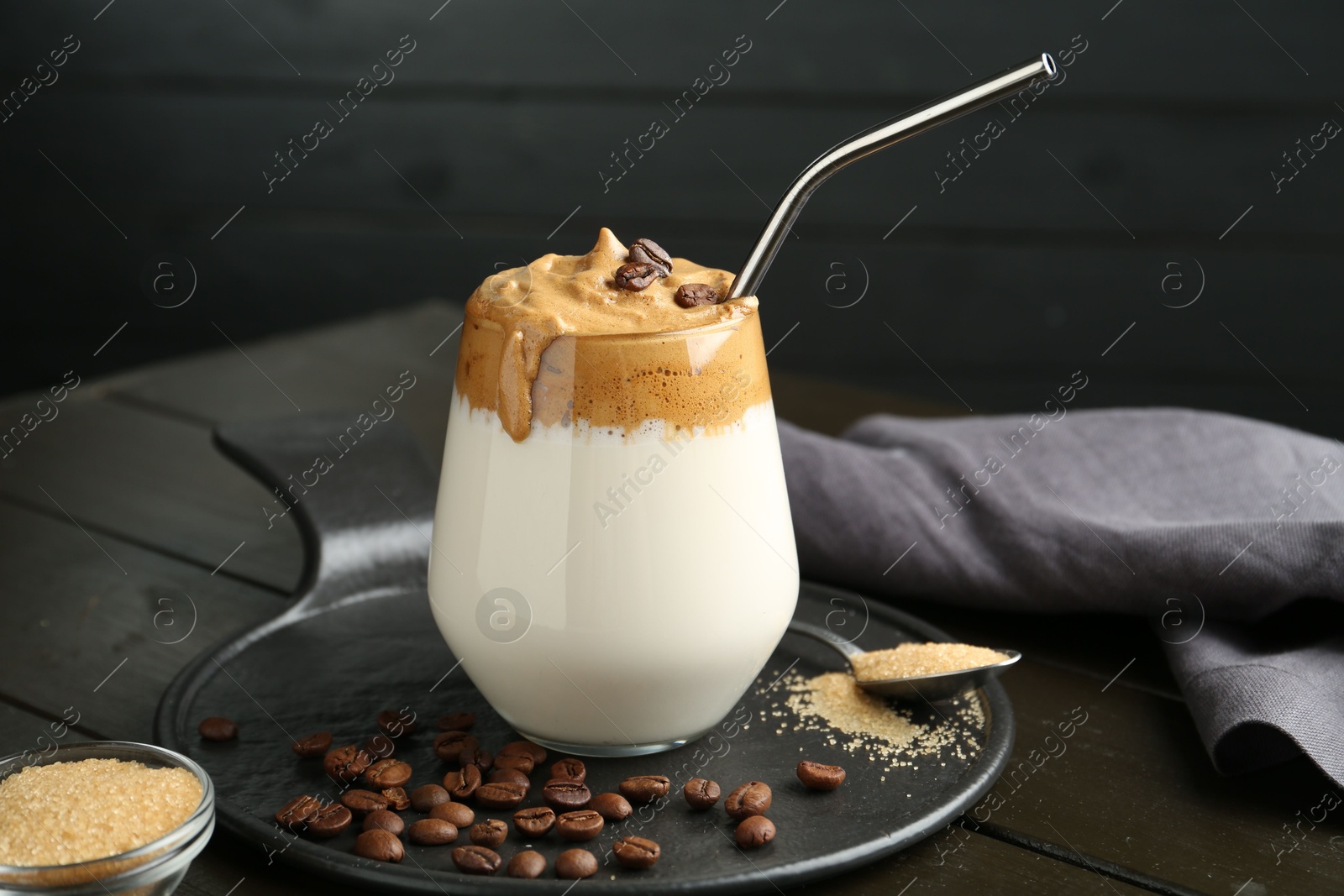 Photo of Delicious dalgona coffee in glass, beans and brown sugar on wooden table, closeup