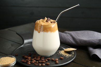 Photo of Delicious dalgona coffee in glass, beans and brown sugar on wooden table, closeup