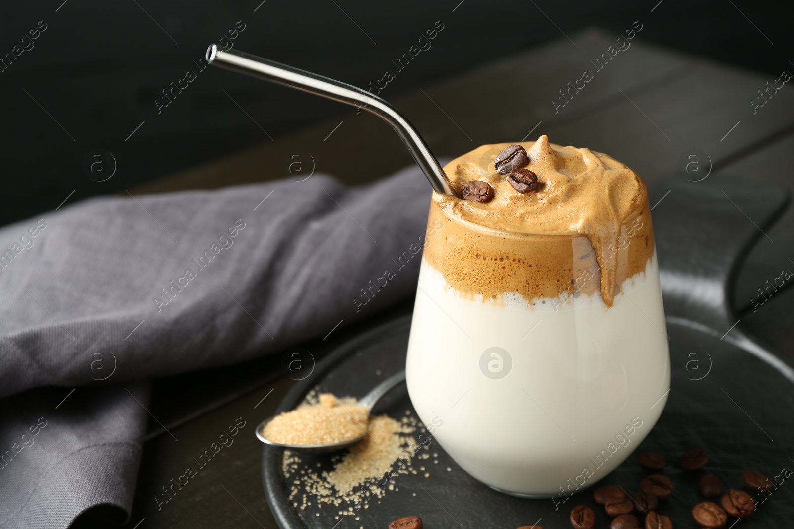 Photo of Delicious dalgona coffee in glass, beans and brown sugar on wooden table, closeup