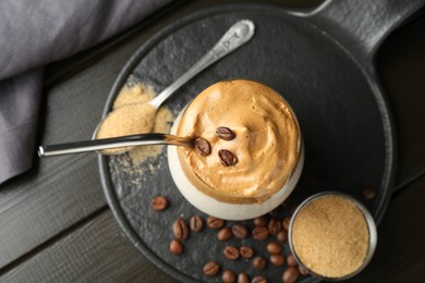 Photo of Delicious dalgona coffee in glass, beans and brown sugar on wooden table, top view