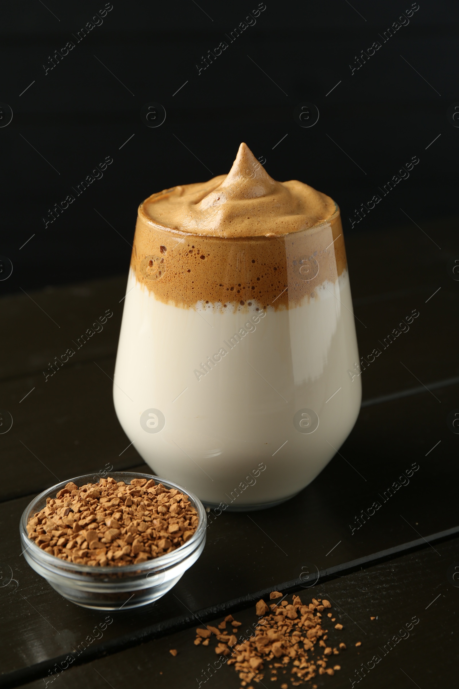 Photo of Delicious dalgona coffee in glass and granules on wooden table, closeup