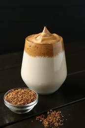 Photo of Delicious dalgona coffee in glass and granules on wooden table, closeup