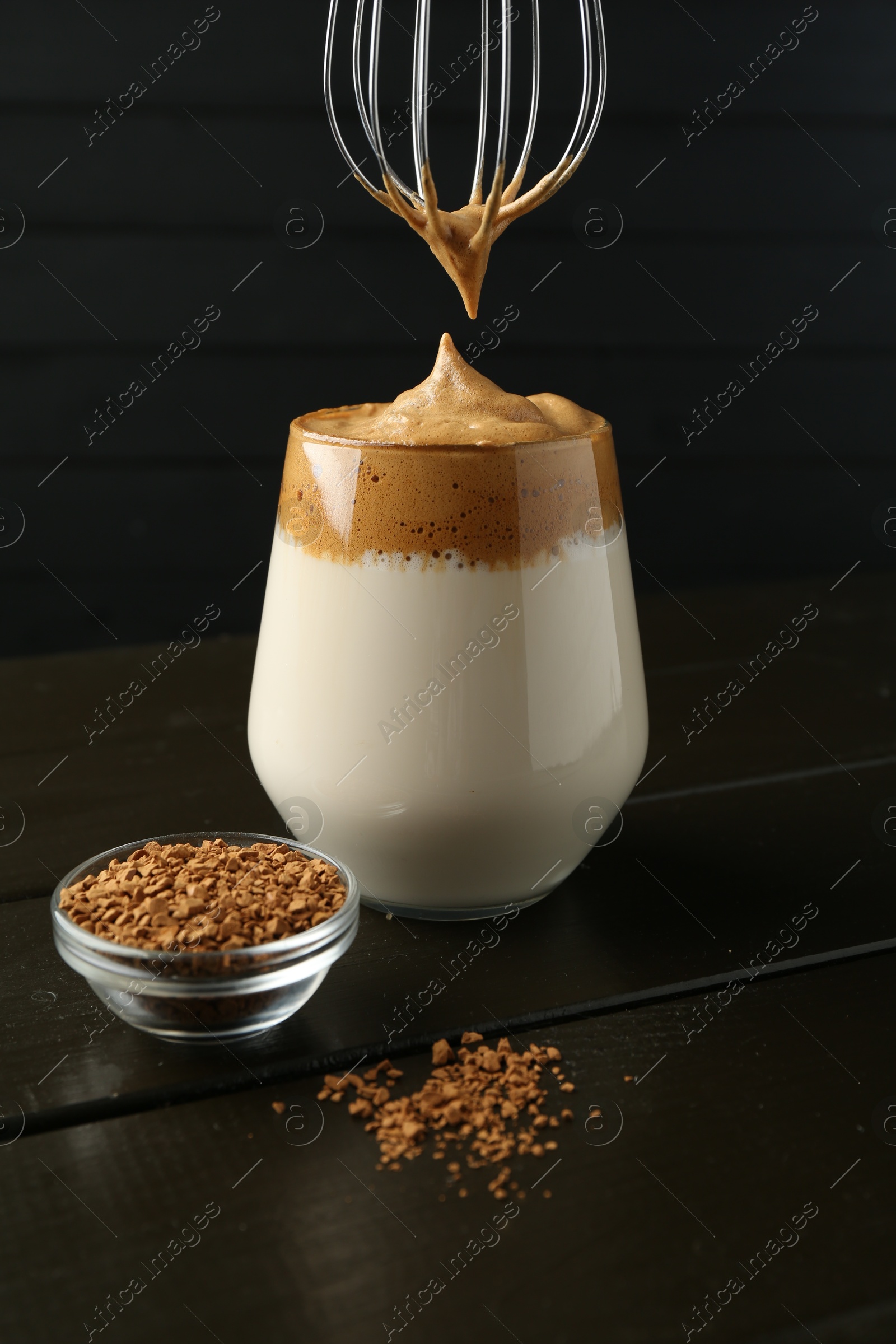 Photo of Pouring cream for dalgona coffee into glass at wooden table, closeup