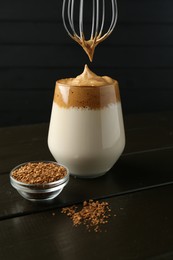 Photo of Pouring cream for dalgona coffee into glass at wooden table, closeup