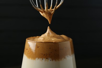 Photo of Pouring cream for dalgona coffee into glass on blurred background, closeup