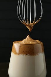 Photo of Pouring cream for dalgona coffee into glass on blurred background, closeup