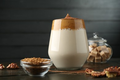 Photo of Delicious dalgona coffee in glass, granules, walnuts and brown sugar on wooden table, closeup