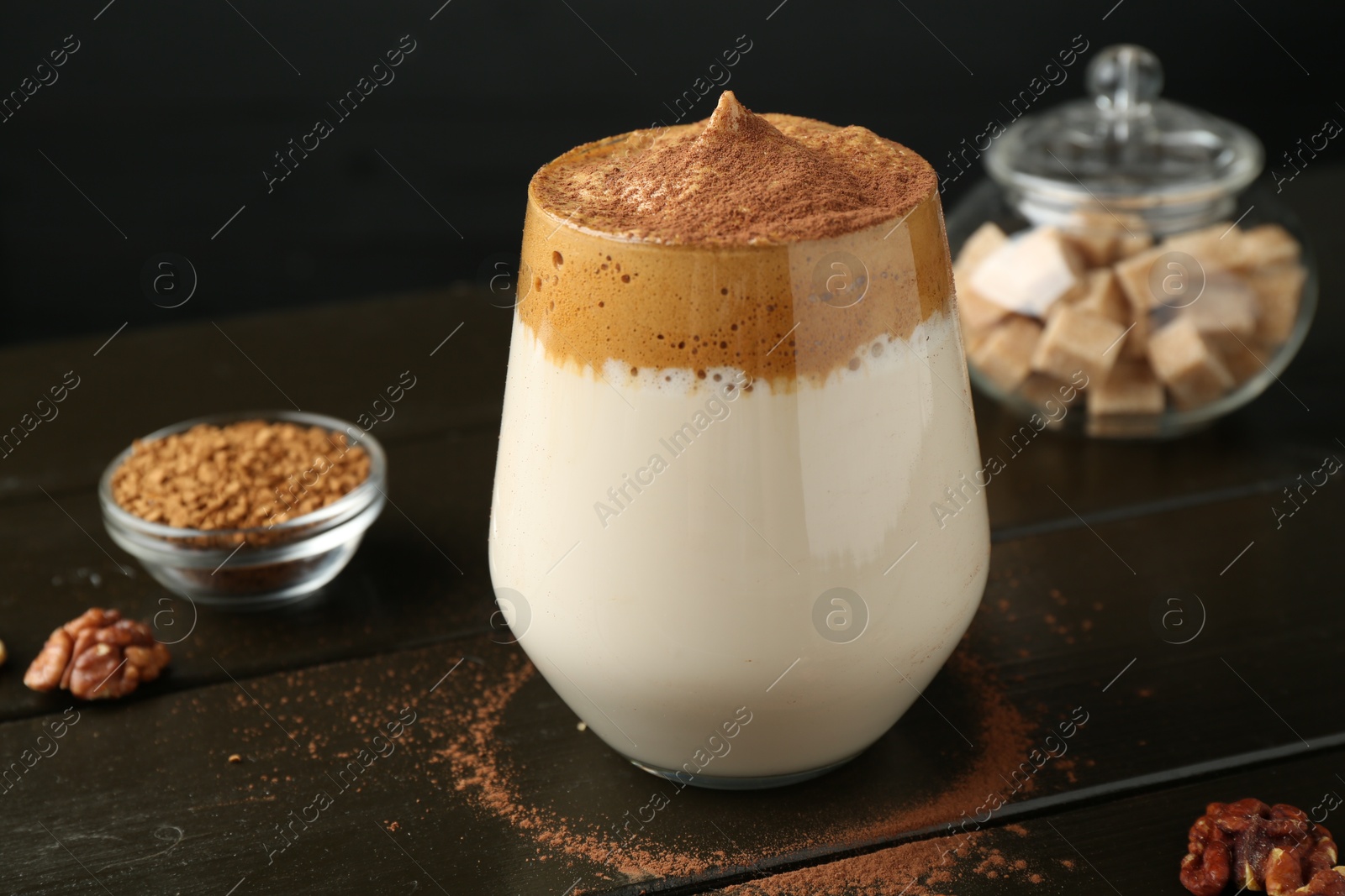 Photo of Delicious dalgona coffee in glass, granules, walnuts and brown sugar on wooden table, closeup