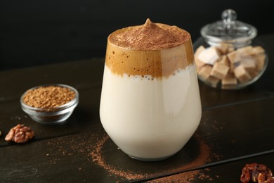 Photo of Delicious dalgona coffee in glass, granules, walnuts and brown sugar on wooden table, closeup