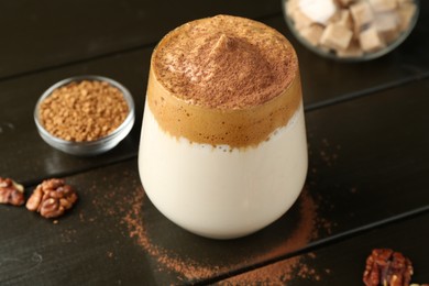 Photo of Delicious dalgona coffee in glass, granules, walnuts and brown sugar on wooden table, closeup