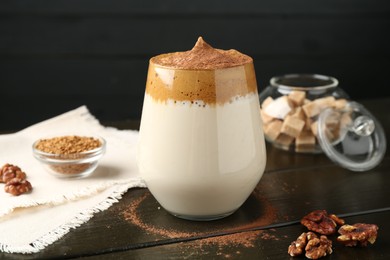 Photo of Delicious dalgona coffee in glass, granules, walnuts and brown sugar on wooden table, closeup