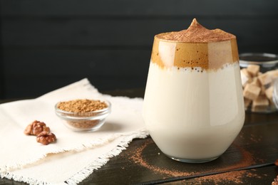 Photo of Delicious dalgona coffee in glass, granules, walnuts and brown sugar on wooden table, closeup