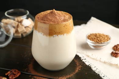 Photo of Delicious dalgona coffee in glass, granules, walnuts and brown sugar on wooden table, closeup