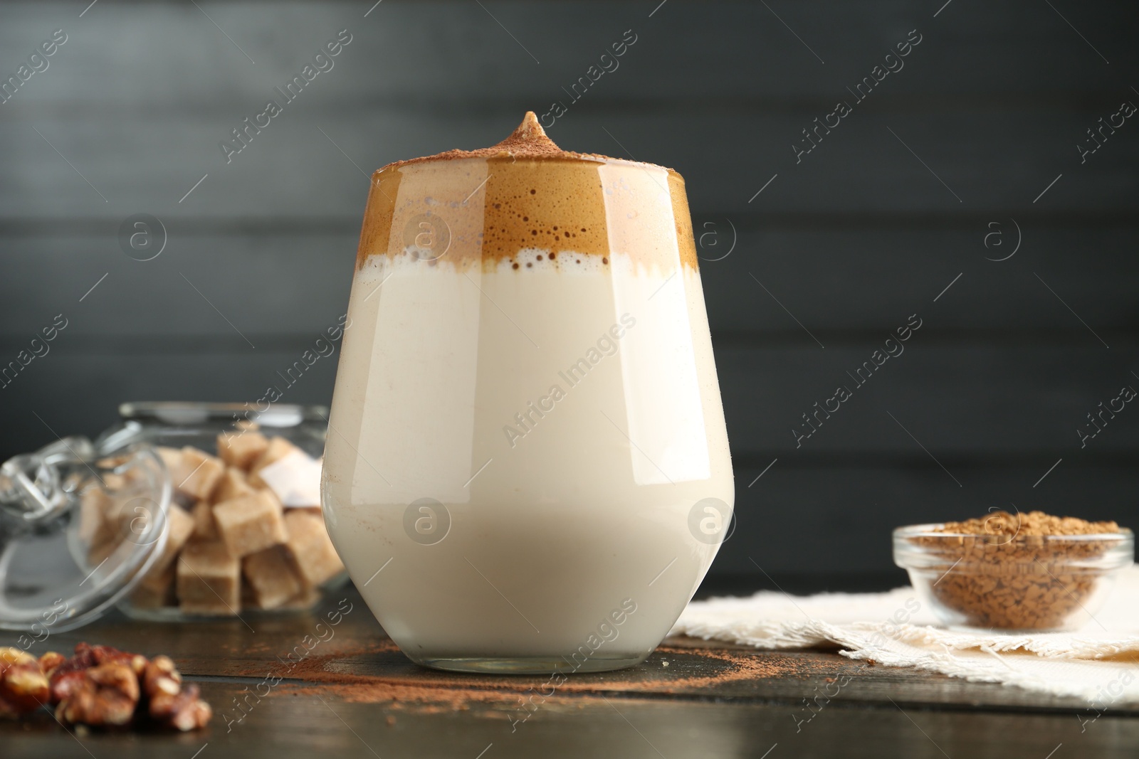 Photo of Delicious dalgona coffee in glass, granules, walnuts and brown sugar on wooden table, closeup
