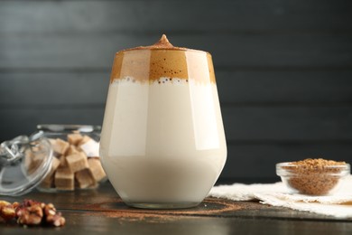 Photo of Delicious dalgona coffee in glass, granules, walnuts and brown sugar on wooden table, closeup