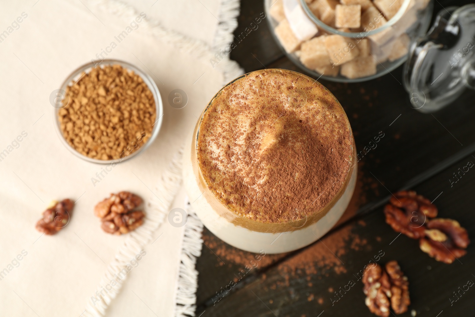 Photo of Delicious dalgona coffee in glass, granules, walnuts and brown sugar on wooden table, flat lay