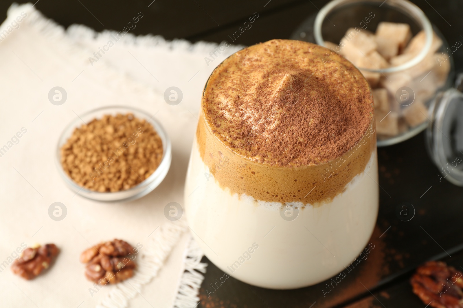 Photo of Delicious dalgona coffee in glass, granules, walnuts and brown sugar on wooden table, above view
