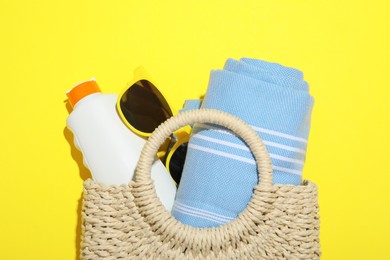 Photo of Wicker bag with beach towel and other summer accessories on yellow background, top view