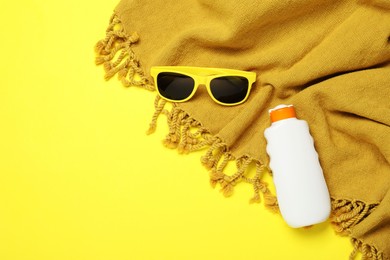Photo of Beach towel, sunglasses and sunscreen on yellow background, flat lay. Space for text