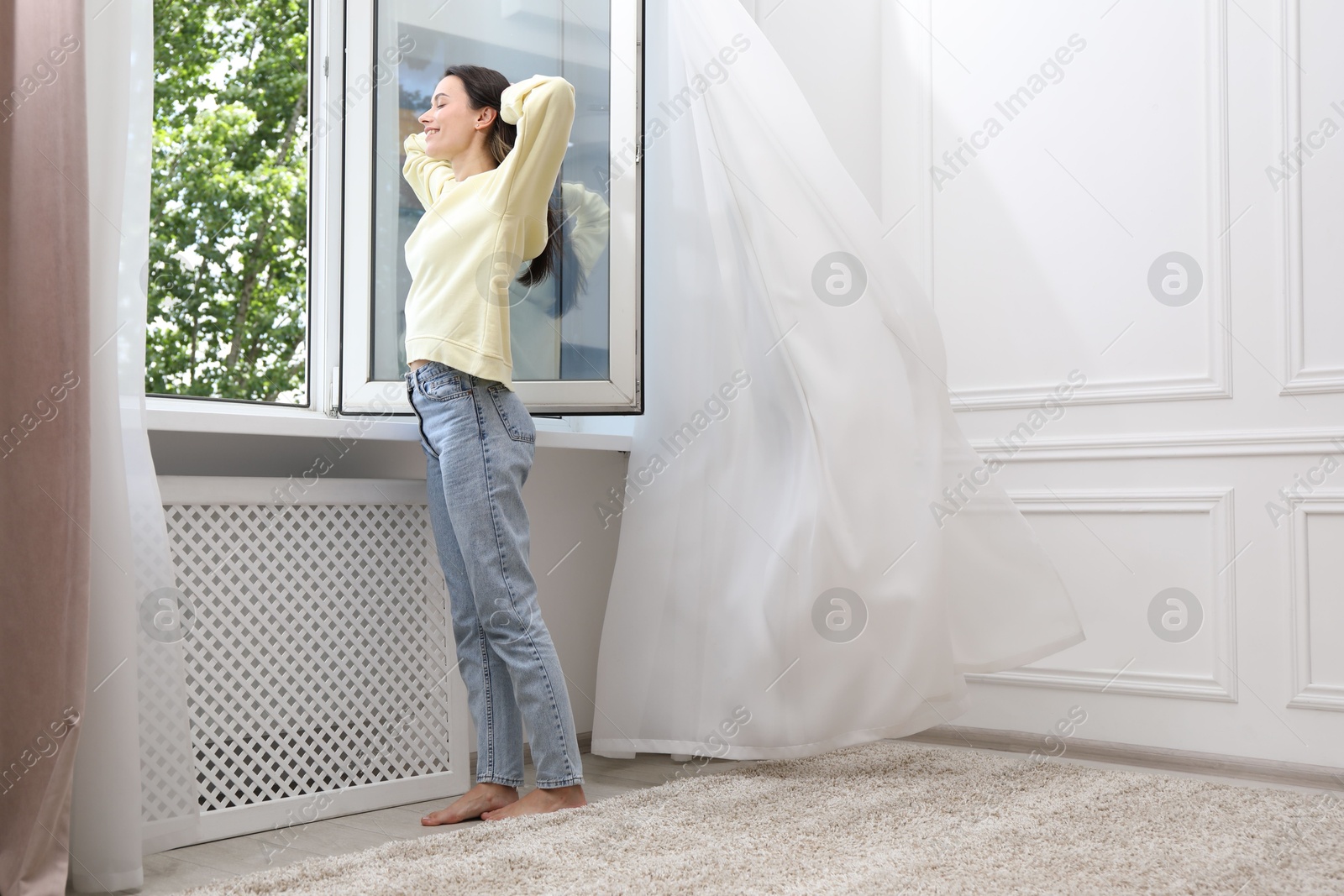 Photo of Harmony. Smiling woman near open window at home, low angle view