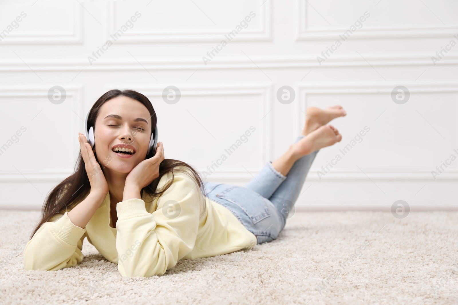 Harmony. Smiling woman in headphones enjoying music on floor near white wall at home Photo of Harmony. Smiling woman in headphones enjoying music on floor near white wall at home