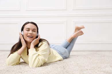 Photo of Harmony. Smiling woman in headphones enjoying music on floor near white wall at home