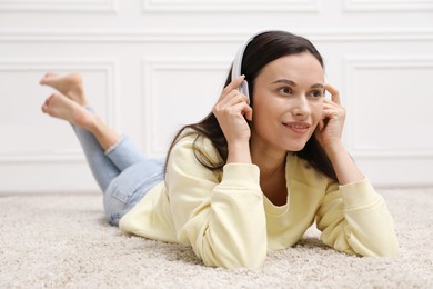 Photo of Harmony. Smiling woman in headphones enjoying music on floor near white wall at home
