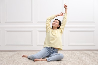 Photo of Harmony. Smiling woman stretching on floor near white wall at home