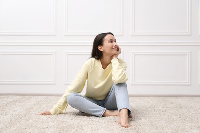 Photo of Harmony. Smiling woman sitting on floor near white wall at home