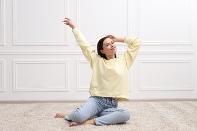 Photo of Harmony. Smiling woman stretching on floor near white wall at home