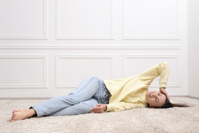Photo of Harmony. Smiling woman lying on floor near white wall at home