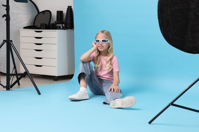 Photo of Little girl on light blue background in photo studio with professional equipment