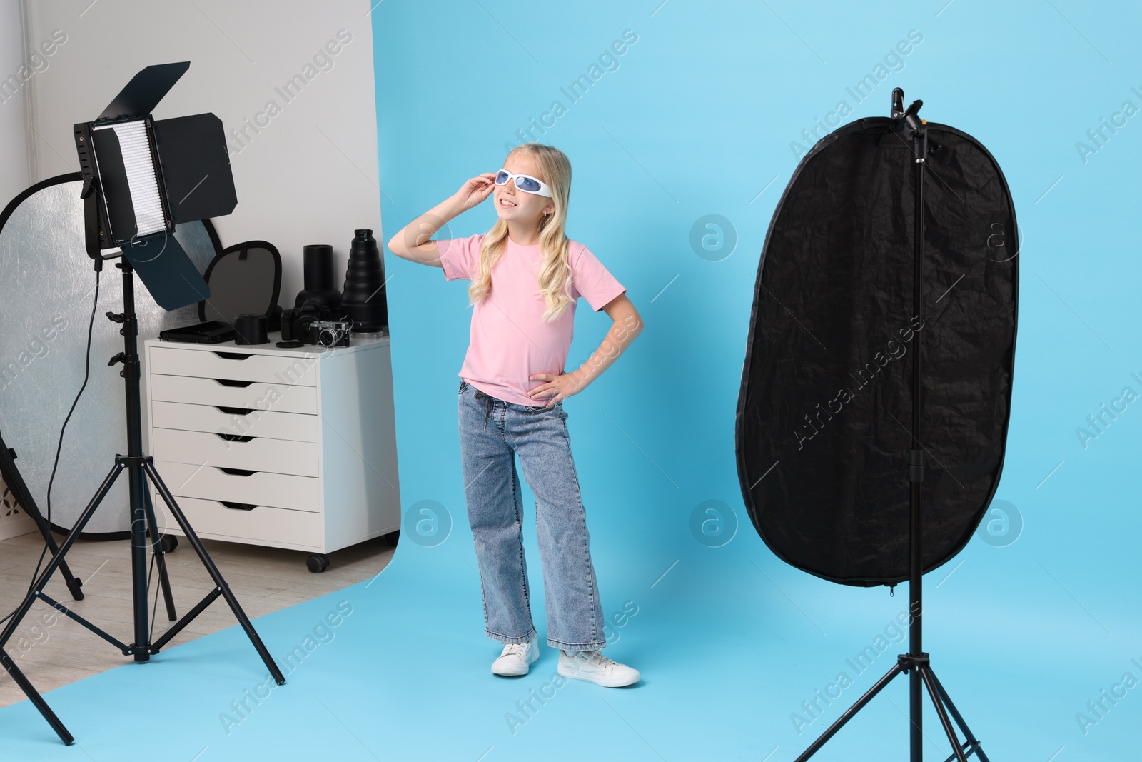Photo of Little girl on light blue background in photo studio with professional equipment