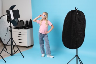 Photo of Little girl on light blue background in photo studio with professional equipment