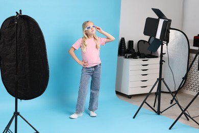 Photo of Little girl on light blue background in photo studio with professional equipment