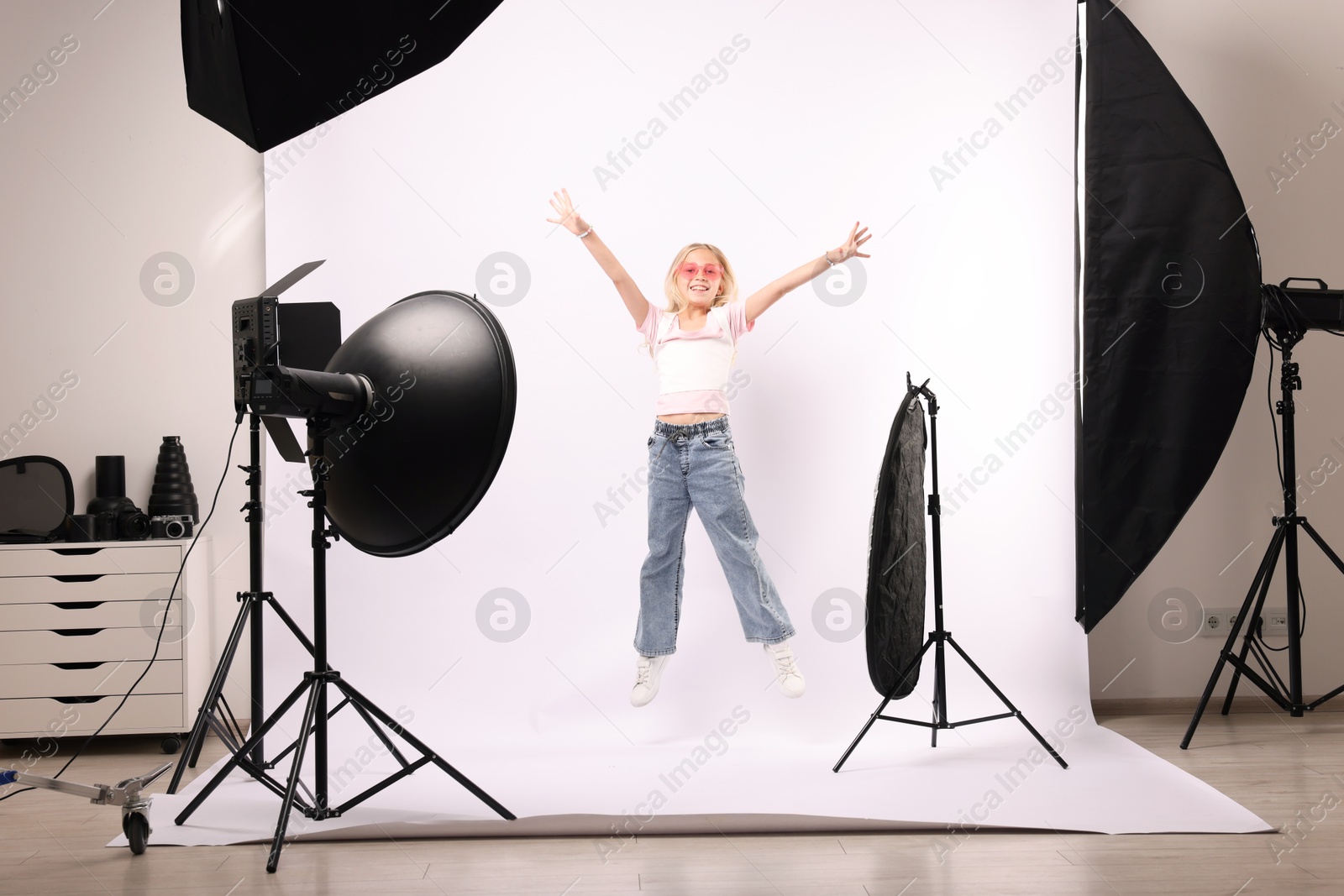 Photo of Little girl jumping on white background in photo studio with professional equipment